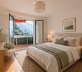 Modern bedroom with a large bed, nightstands, a chair, and a scenic view of mountains through large windows.