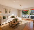 Modern living room with light-colored sectional sofa, wooden coffee table, side tables, floor lamp, and large windows opening to a balcony.