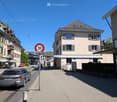 Urban street with a speed limit sign, buildings, parked cars, and pedestrians.