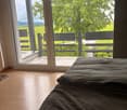 Bedroom. Bright bedroom with wooden flooring, large windows offering a scenic view of green fields and trees, and a single bed with dark bedding.