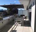 Balcony with a tiled floor, a white table and chairs, an umbrella, and a view of the city and mountains.