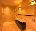 Modern bathroom with a sleek sink, toilet, large mirror, and glass-enclosed shower. Warm lighting and marble tiles.