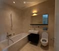 Modern bathroom with beige tiles, a bathtub, a sink with a black cabinet, a toilet, and a large mirror above the sink.