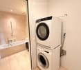 A modern bathroom with a bathtub, showerhead, and a stacked washer and dryer unit.