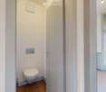 Bathroom. Small bathroom with a toilet, wooden floor, white walls, and a frosted glass window with a view of greenery.