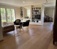 Living Room. Spacious living room with hardwood floors, large windows, a sofa, chairs, a small round table, a bookshelf, and a television.