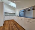 modern kitchen with white cabinets, wooden floor, two blue double ovens, a window, and a skylight