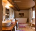Bathroom. Bathroom with wooden ceiling beams, a large freestanding bathtub, two sinks, a mirror, a towel rack, and a small wooden chair with a towel draped over it.