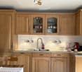 Kitchen. A well-lit kitchen with light wooden cabinets, a stainless steel sink, and a coffee maker on the counter. The backsplash features a decorative tile design with coffee and chocolate motifs.