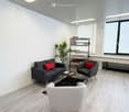 Furnished Room. Modern living room with grey sofa, red throw pillow, grey armchair, coffee table, bookshelf, and a small plant. Light wood flooring and white walls.