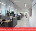 Furnished Room. Modern office space with desks, chairs, computers, and plants. The room features a clean, organized layout with large windows providing natural light.