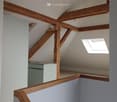 Corridor / Hallway. Staircase with wooden handrail and exposed wooden beams, light blue walls, skylight window providing natural light.