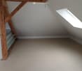 Unfurnished Room. Empty attic space with wooden beams, skylight window, and built-in shelving unit.