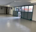 Empty room with white walls, white floor, large windows, and a door leading to an outdoor area.