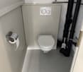 small bathroom with toilet, wall mounted toilet paper holder, and pipes