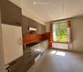 Kitchen. A small, unfurnished kitchen with wooden cabinets, a white refrigerator, a sink, and an oven. The space features a retro orange backsplash and a window with striped curtains.