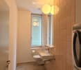 Bathroom. Modern bathroom with beige tiles, a toilet, a sink with a modern faucet, a washing machine, and a large mirror with integrated lighting.