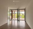 Unfurnished Room. Empty hallway with tiled floor, light-colored walls, and large glass doors leading to a balcony with a view of greenery and buildings.