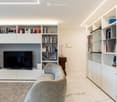 Furnished Room. Modern living room with built-in white bookshelves, a grey sofa, a flat-screen TV, a small wooden side table with a lamp, and decorative items on the shelves.
