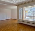 Empty room with wooden flooring, white walls, large window with blinds, and a radiator below the window.