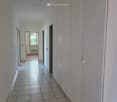 Empty hallway with white tiles, white walls, white cabinets, and a window with a view of trees.