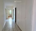Empty hallway with tiled floor and white walls, featuring several doors and a visible room at the end with a window and radiator.
