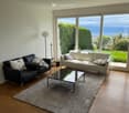 modern living room with two black leather sofas, white leather sofa, glass coffee table, floor lamp, carpet, large windows with view of the sea