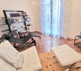 Furnished Room. Modern living room with a white leather sofa, ottoman, a black lounge chair, a bookshelf filled with books, and a large screen on a stand.