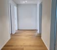Corridor / Hallway. Empty hallway with light wooden flooring, white walls, and several doors leading to other rooms.