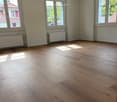 Unfurnished Room. Empty room with wooden flooring, large windows, radiators, and natural light. No furniture or equipment present.