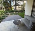 Balcony / Terrace. Balcony with a grey sofa, a round table, and a view of a garden and trees.