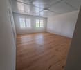 Unfurnished Room. Empty room with wooden flooring, white walls, and large windows allowing natural light. No furniture or equipment present.