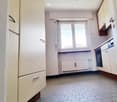Kitchen. Empty kitchen with white cabinets, a refrigerator, and an oven. The floor is tiled, and there is a window with a radiator below it.