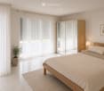 Modern bedroom with a wooden bed, nightstand, lamp, large mirror, plant, and picture frame on the wall.