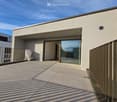 Balcony / Terrace. Modern balcony with tiled floor, glass sliding doors, metal railing, and a view of the building entrance.