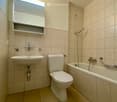 Bathroom. Modern bathroom with beige tiles, a sink, toilet, bathtub, and a built-in shelf above the sink.