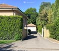 House. A two-story house with a tiled roof, beige exterior, and a well-maintained hedge-lined driveway leading to a garage.