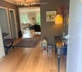 Corridor / Hallway. Spacious hallway with wooden flooring, leading to a living room area with a sofa, armchair, and coffee table. Features a side table with a lamp, decorative vases, and a painting on the wall.
