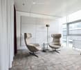 Furnished Room. Modern living room with two beige armchairs, a small round table, and a floor lamp, featuring large windows and a neutral color palette.