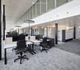 Furnished Room. Modern office space with desks, chairs, computer monitors, and lockers, featuring large windows and a carpeted floor.