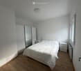 Bedroom. Minimalist bedroom with a white bed, wooden flooring, and a large mirror on the wardrobe.