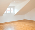 Unfurnished Room. Empty room with wooden flooring, white walls, and a slanted ceiling. Two windows are visible on one wall.