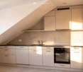 Kitchen. Modern kitchen with light-colored cabinets, a sink, a faucet, and an oven, featuring a slanted ceiling and tiled floor.