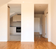 Unfurnished Room. Empty hallway with wooden flooring, white walls, and open doorways leading to a kitchen and another room.