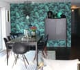 Modern dining and living area with a dark green leafy wallpaper, a sleek dining table with black chairs, a grey sofa, and a cabinet with decorative items on top.