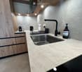 Modern kitchen with a marble countertop, stainless steel sink, black faucet, and wooden cabinets.