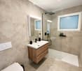 Bathroom. Modern bathroom with beige tiles, a white toilet, a wooden vanity with a sink, a large mirror, and a glass-enclosed shower with a modern showerhead.