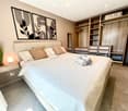 Bedroom. Modern bedroom with a large bed, nightstand, lamp, mirror, and built-in wardrobe with drawers. Features decorative wall art and a potted plant on the nightstand.