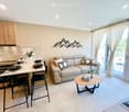 Furnished Room. Modern open-plan living and dining area with a cream sofa, coffee table, dining table with stools, kitchen area with cabinets and appliances, and decorative wall art.
