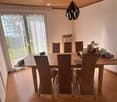Dining room with a wooden table, six chairs, laptop, cups, radiator, and decorative items on the table.